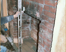 A man working on a brick fireplace in an unfinished room.