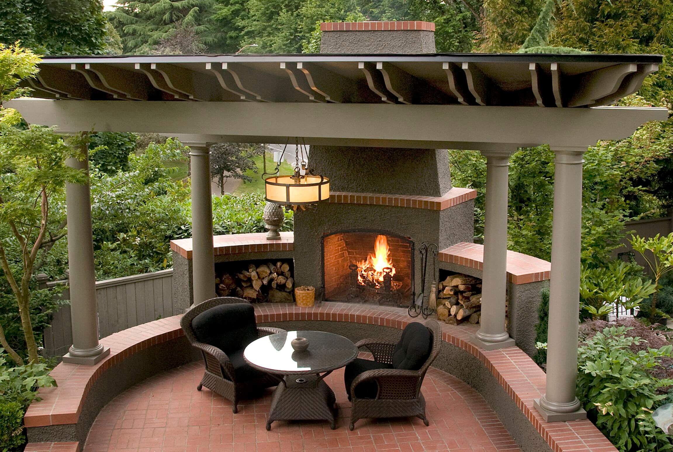 Two outdoor chairs and a table sitting near a lit fireplace.