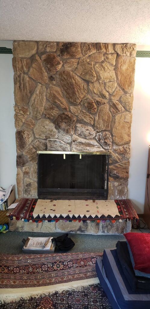 Stone fireplace with a closed black firebox and decorative rugs in front.