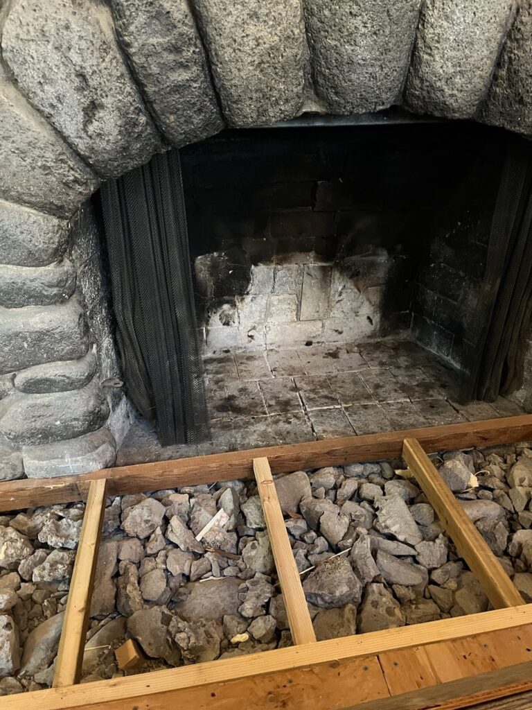 Empty Portland stone fireplace with a metal screen, surrounded by a wooden frame filled with rocks.