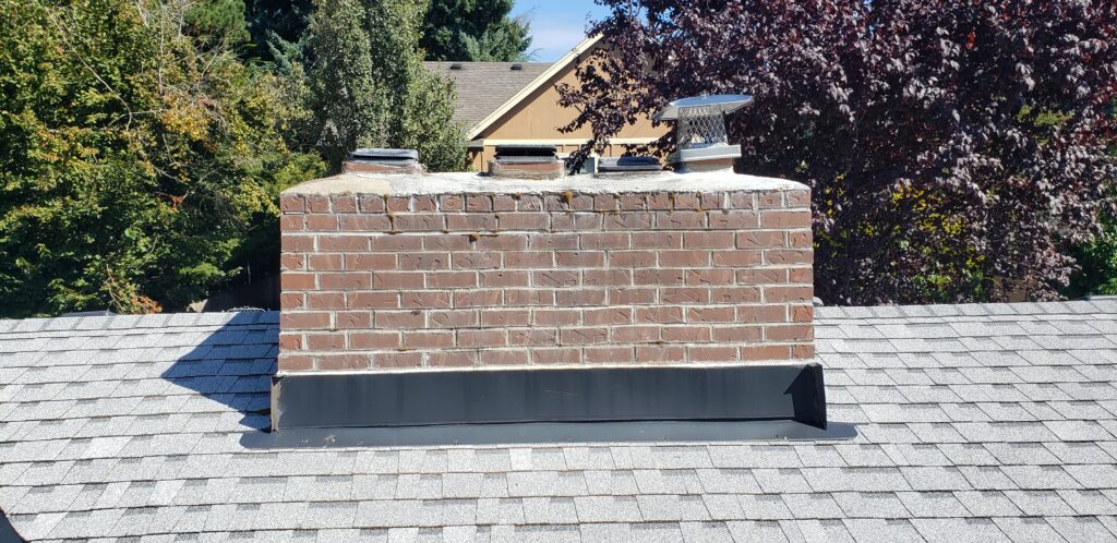 Brick chimney on a house roof with asphalt shingles on a sunny day.