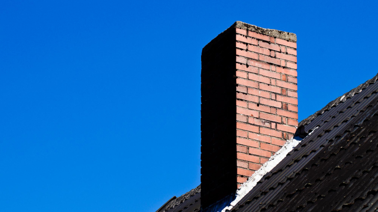 A red brick chimney stands atop a sloped, shingled roof against a clear blue sky.