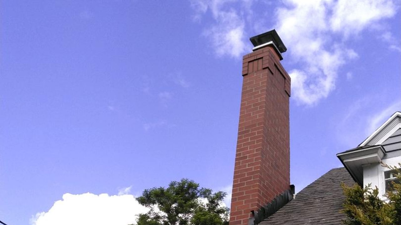 Brick chimney on a house with a clear blue sky and a few clouds in the background.