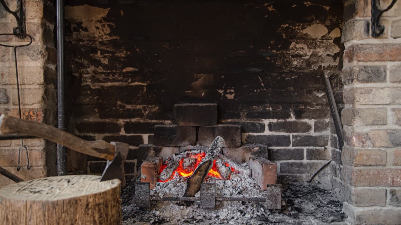 A brick fireplace with glowing embers, an axe and a log are nearby.