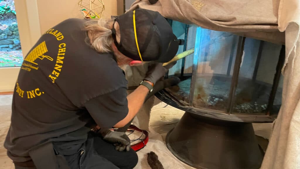 Technician cleaning a chimney with a brush; wearing a black shirt and cap.