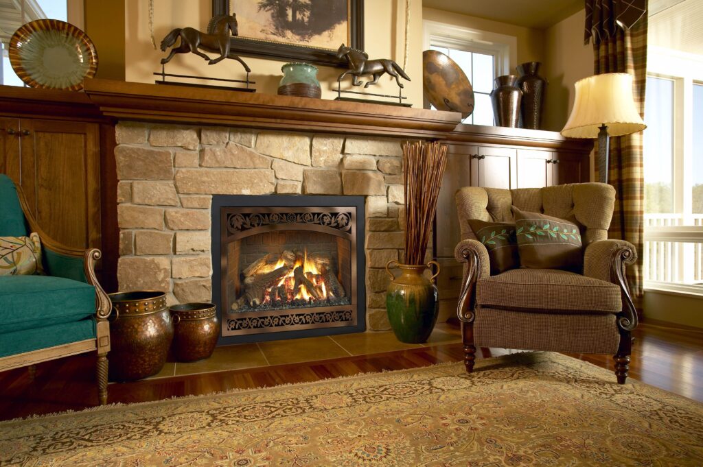 A cozy living room with a stone fireplace, armchair, and decorative items on the mantel, including a framed picture and pottery. Sunlight streams through a large window.