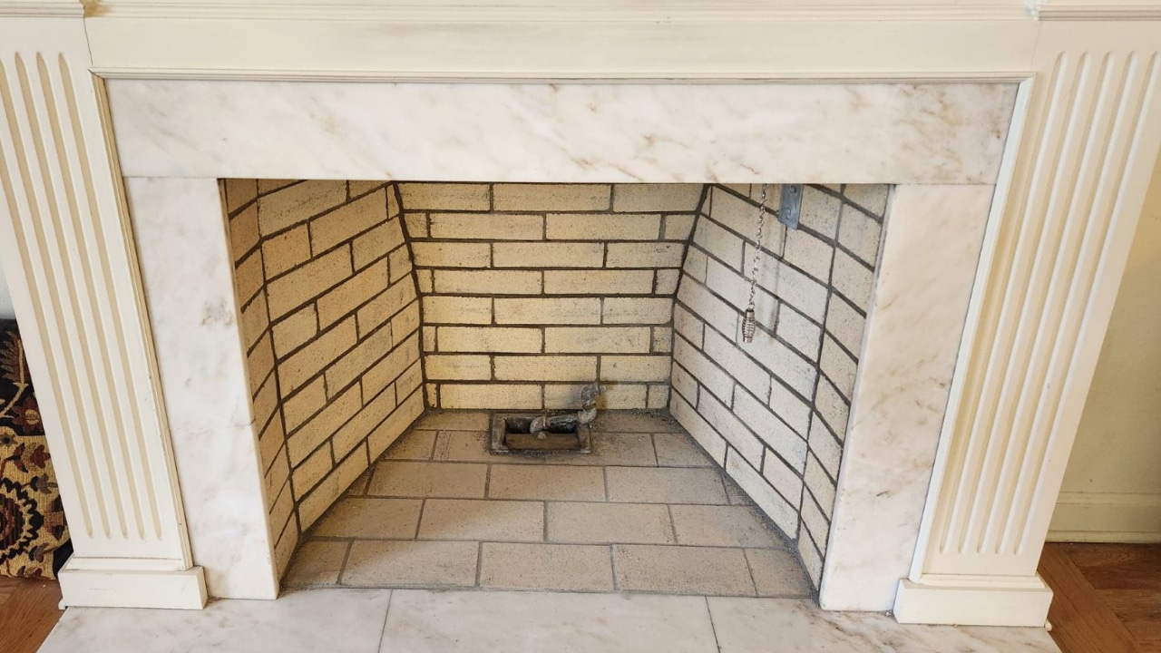 A white marble fireplace with a brick-lined interior and a metal gas burner installed at the center.