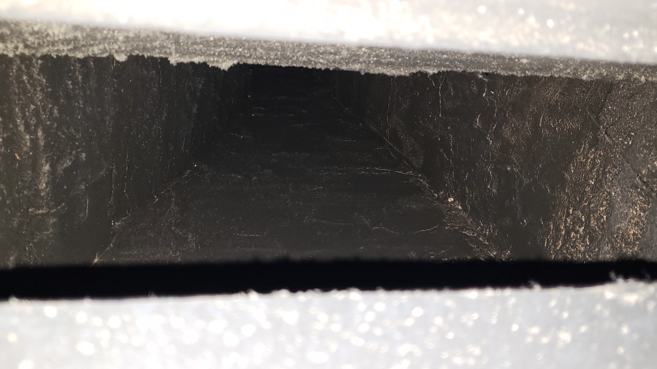 A dark, narrow interior view of an air duct with visible dust and cobwebs.