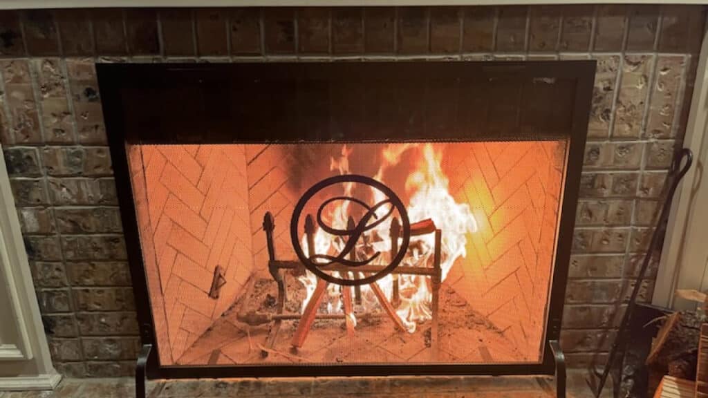 A fireplace with a metal screen in front of burning logs, enclosed by a brick surround.