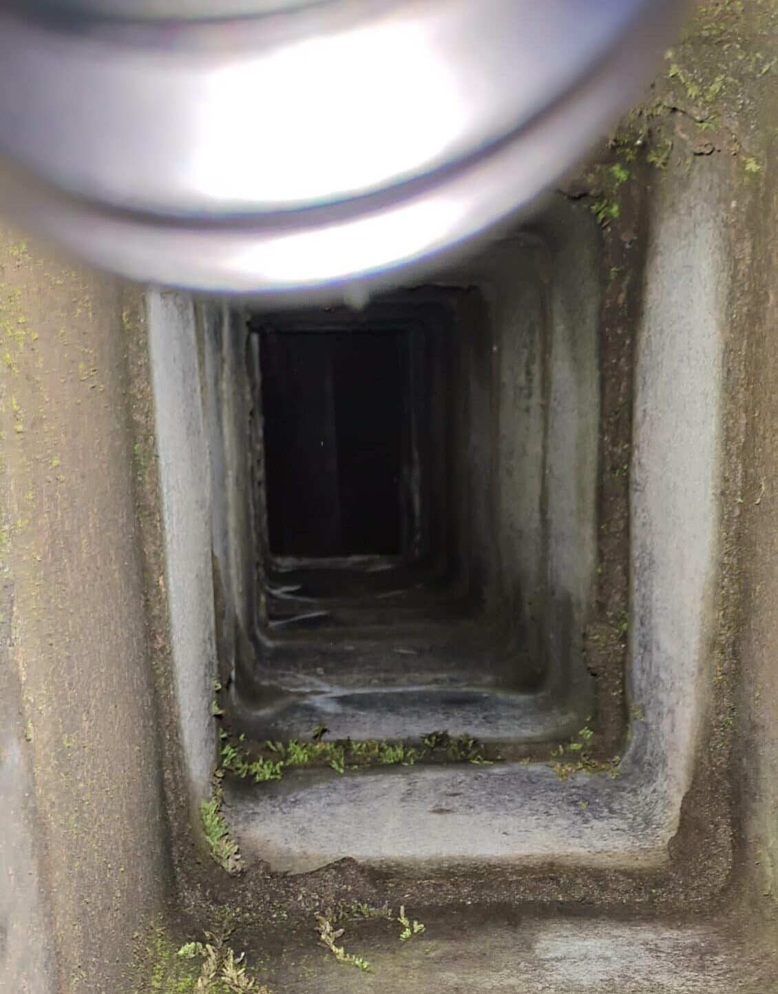 View inside a rectangular concrete or stone tunnel with moss and dirt on the walls; a metallic, rounded object is partially visible at the top edge.