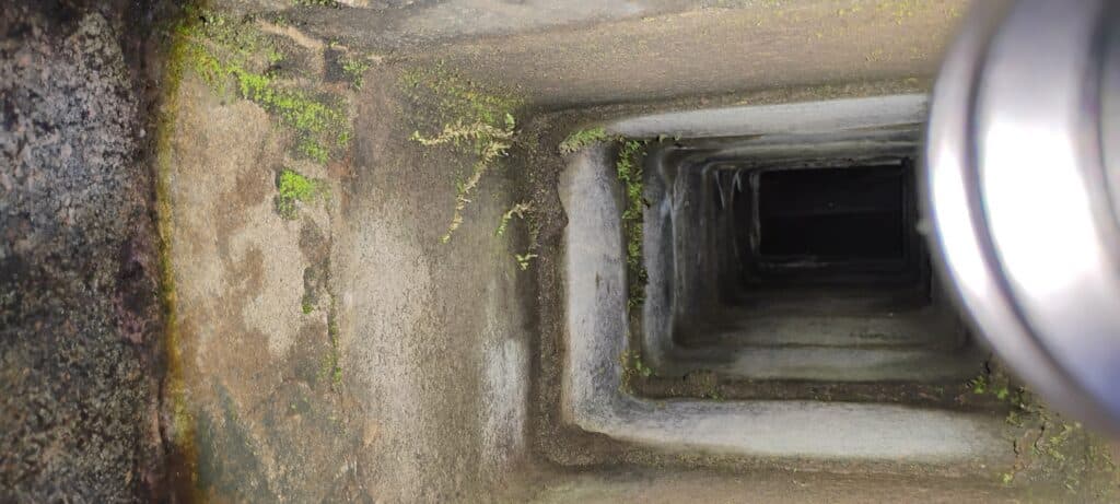 View looking down a square, moss-covered concrete shaft with a cylindrical metal object visible on the right edge.