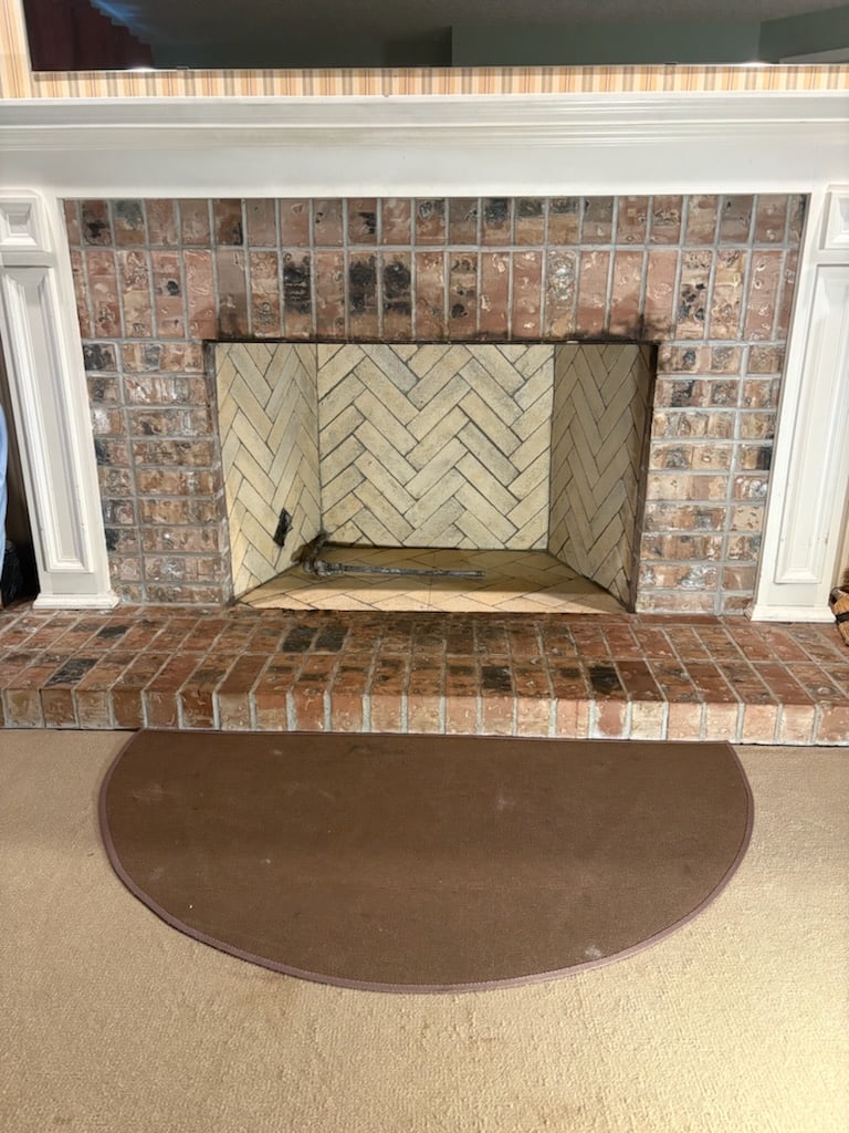 A fireplace with a brick hearth and a rug.