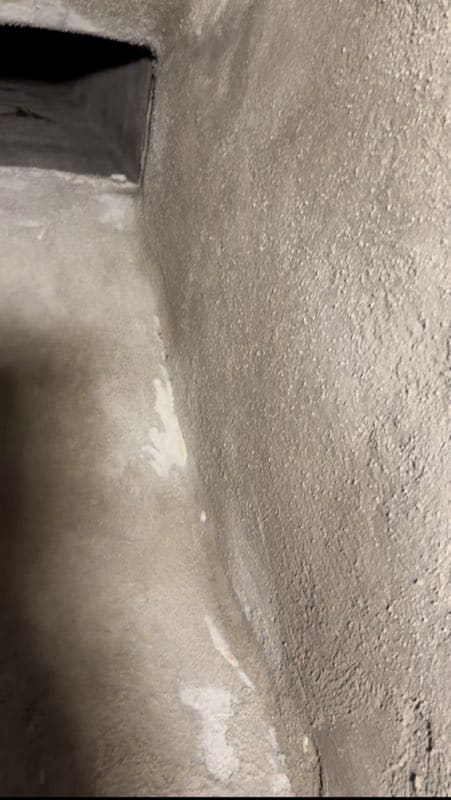 A close-up view of the inside of an air duct or vent, showing textured, dusty walls and a rectangular opening in the background.