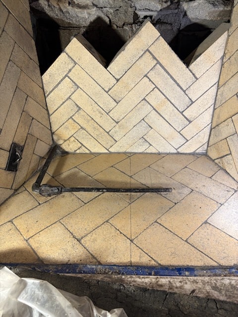 A brick oven with a herringbone tile pattern on the floor and back wall, containing a metal tool resting inside.