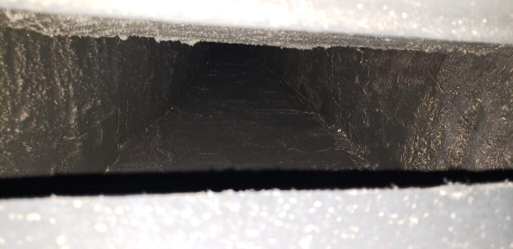 Close-up view inside a dark, dusty ventilation duct with visible dust and debris along the inner surfaces.